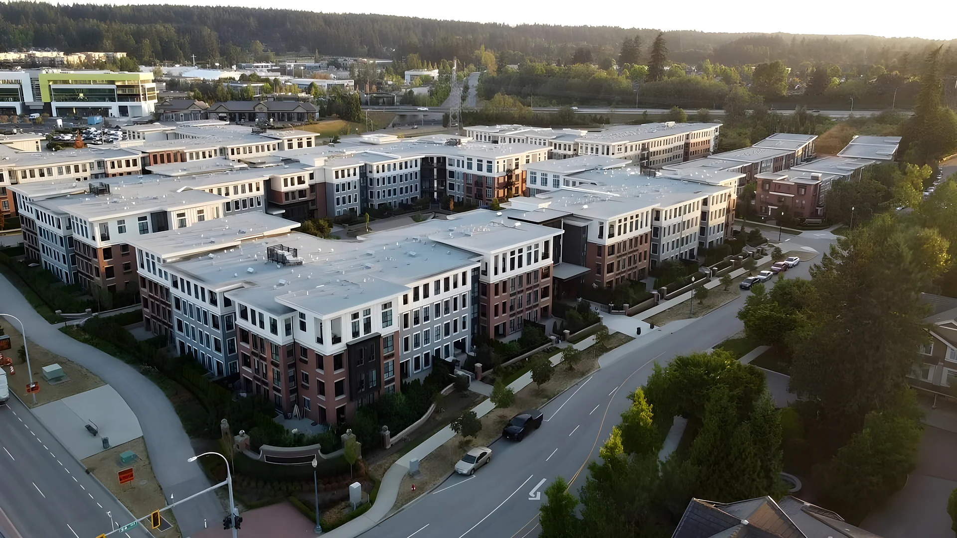 Aerial view of a large townhouse and apartment complex beside a road with trees