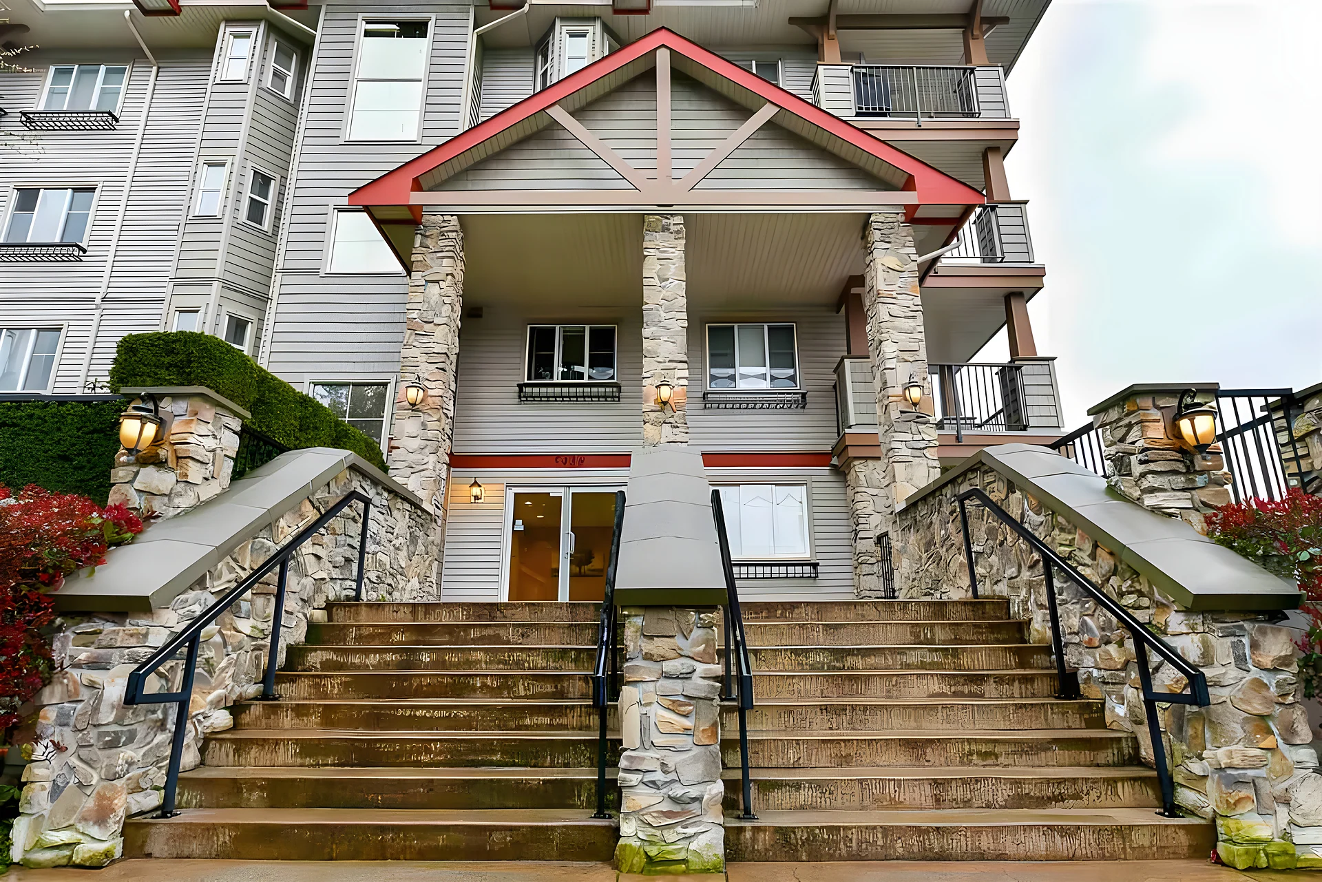 Multi-unit residential building with stone pillars, wide stone staircase and red-roofed gable entry