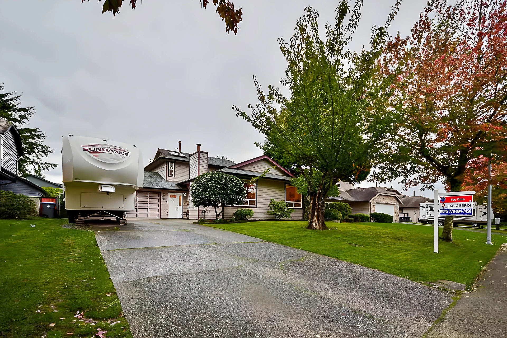 Single-storey house with driveway, large trees, a parked RV trailer and a For Sale sign on an overcast day