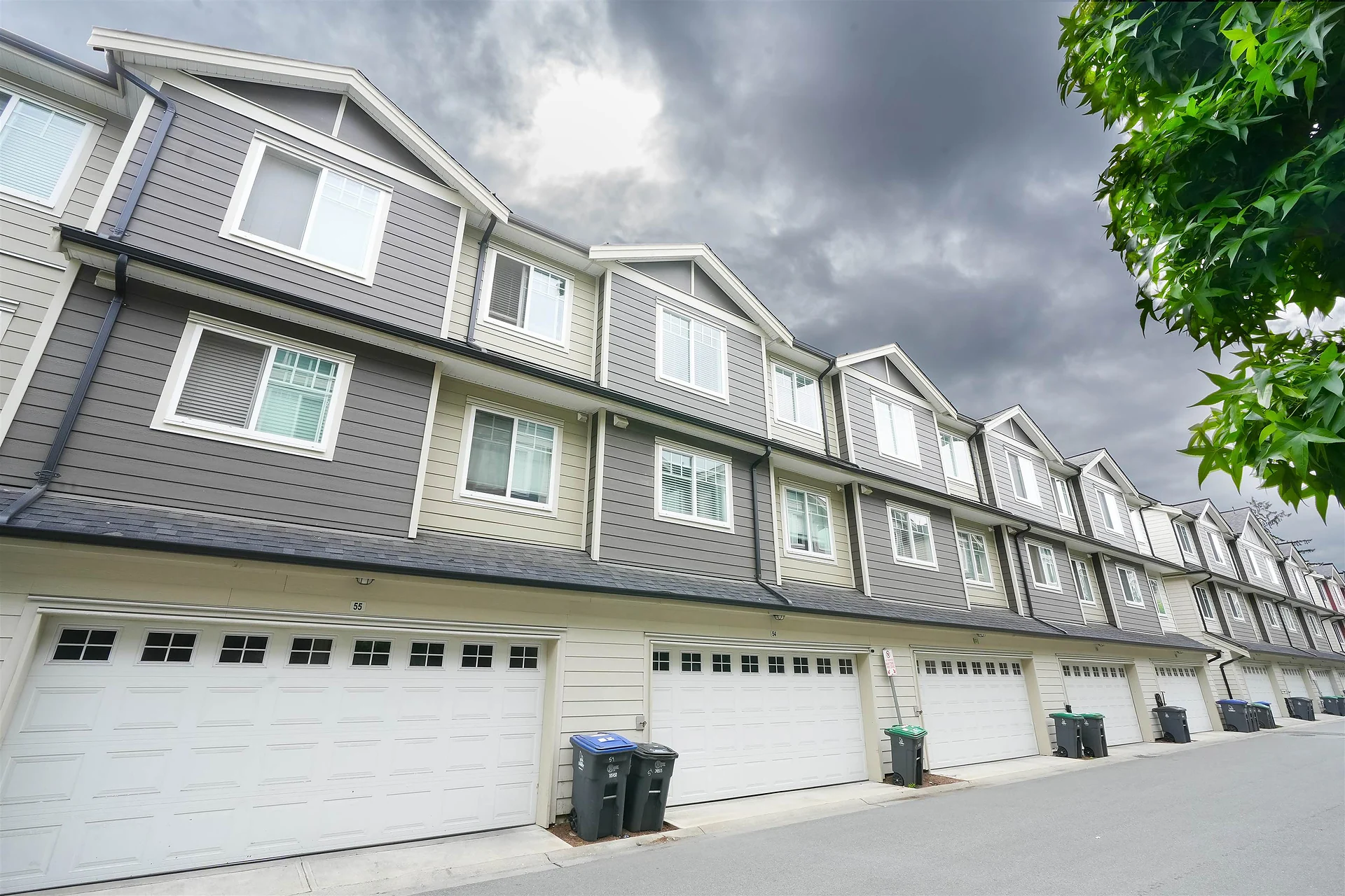 Long row of grey three-storey townhouses with garage doors, low wide-angle view of the rear laneway side