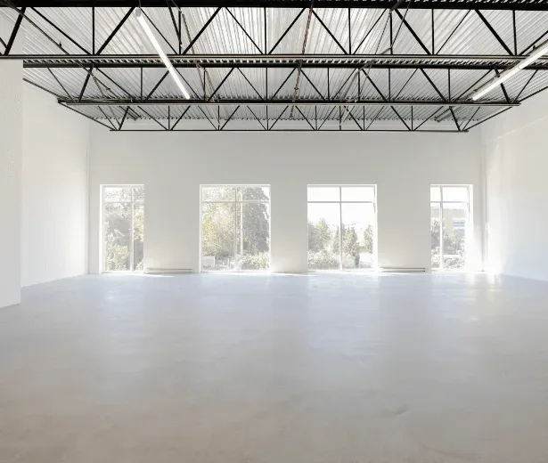 Large empty industrial unit with steel roof trusses, a concrete floor and tall windows