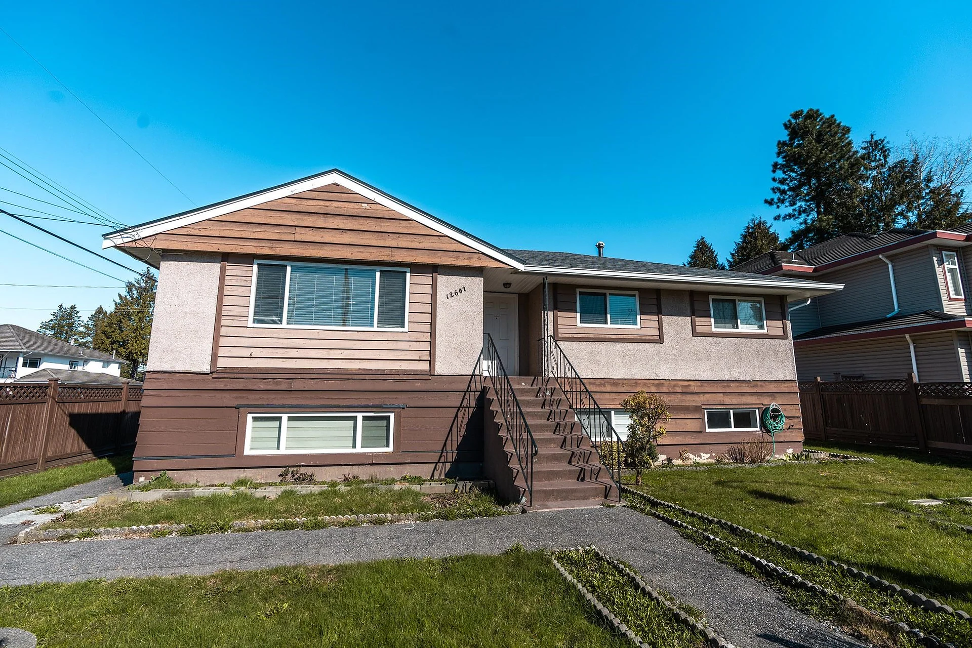 Single-storey brown house with stairs, lawn and bright blue sky