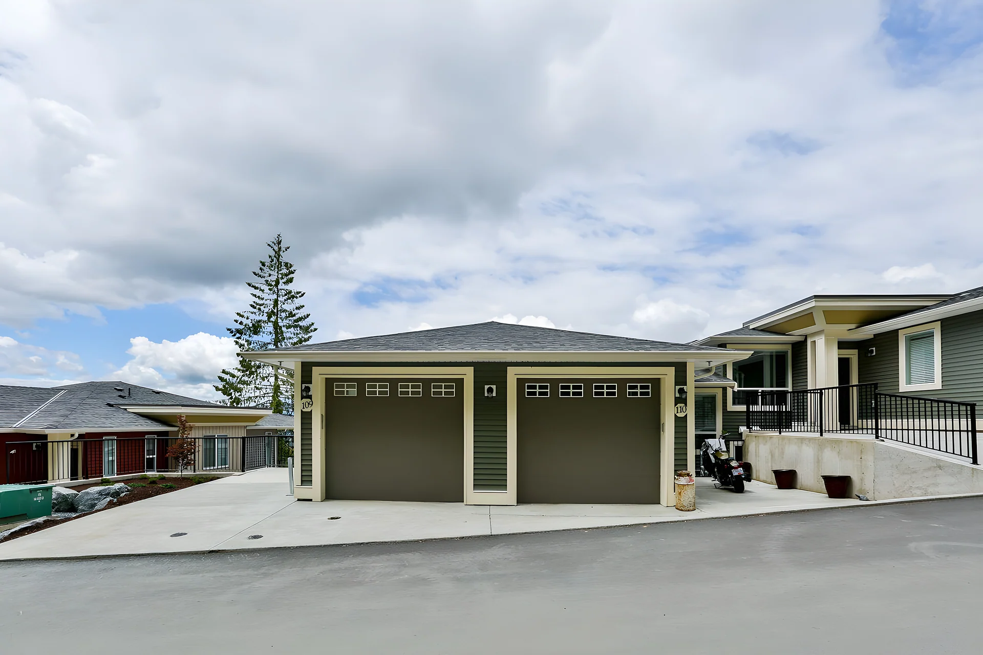 Detached double garage with tan doors in front of a rancher-style home on a hillside street