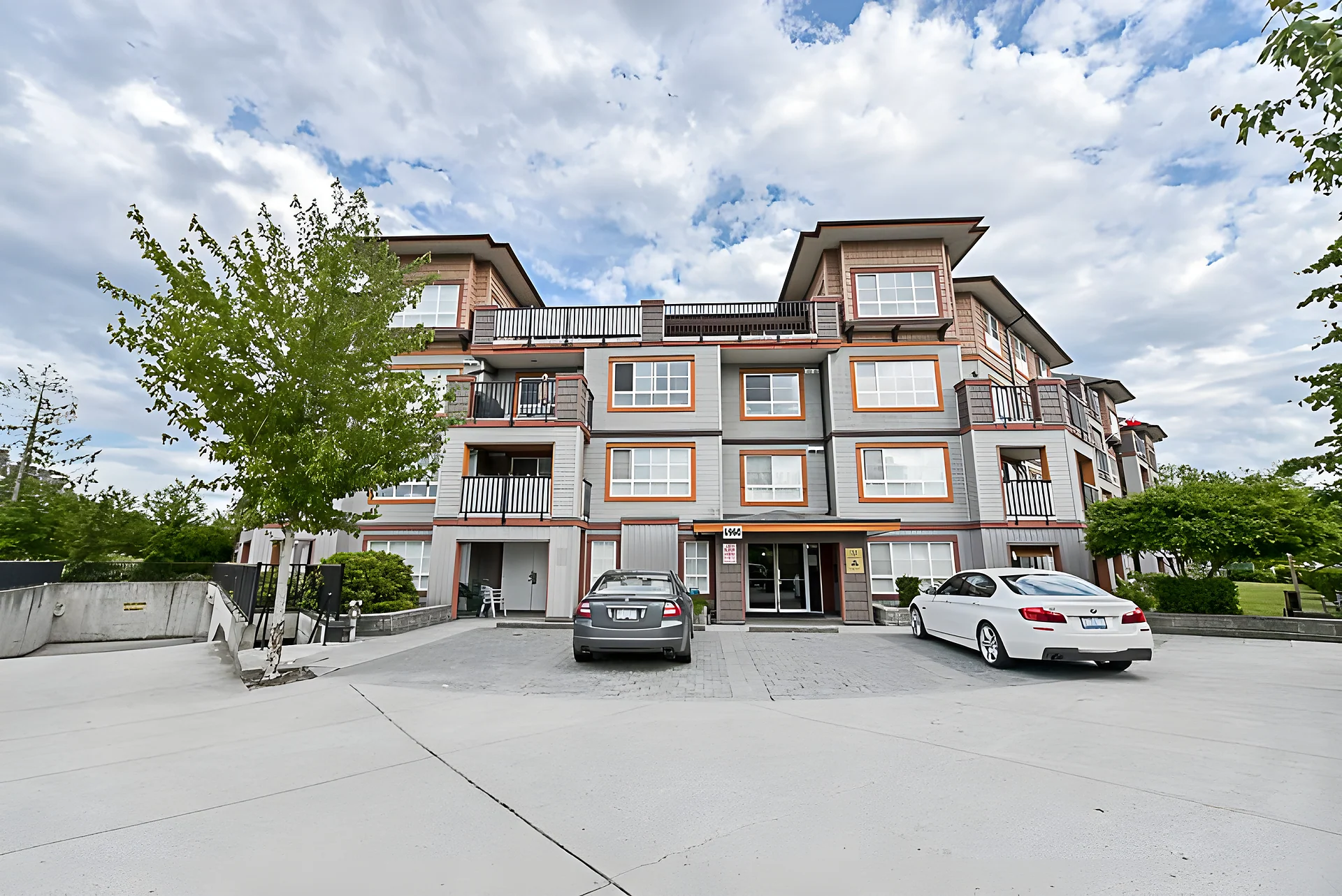 Three-storey income property with a paved parking area and two cars under a partly cloudy sky