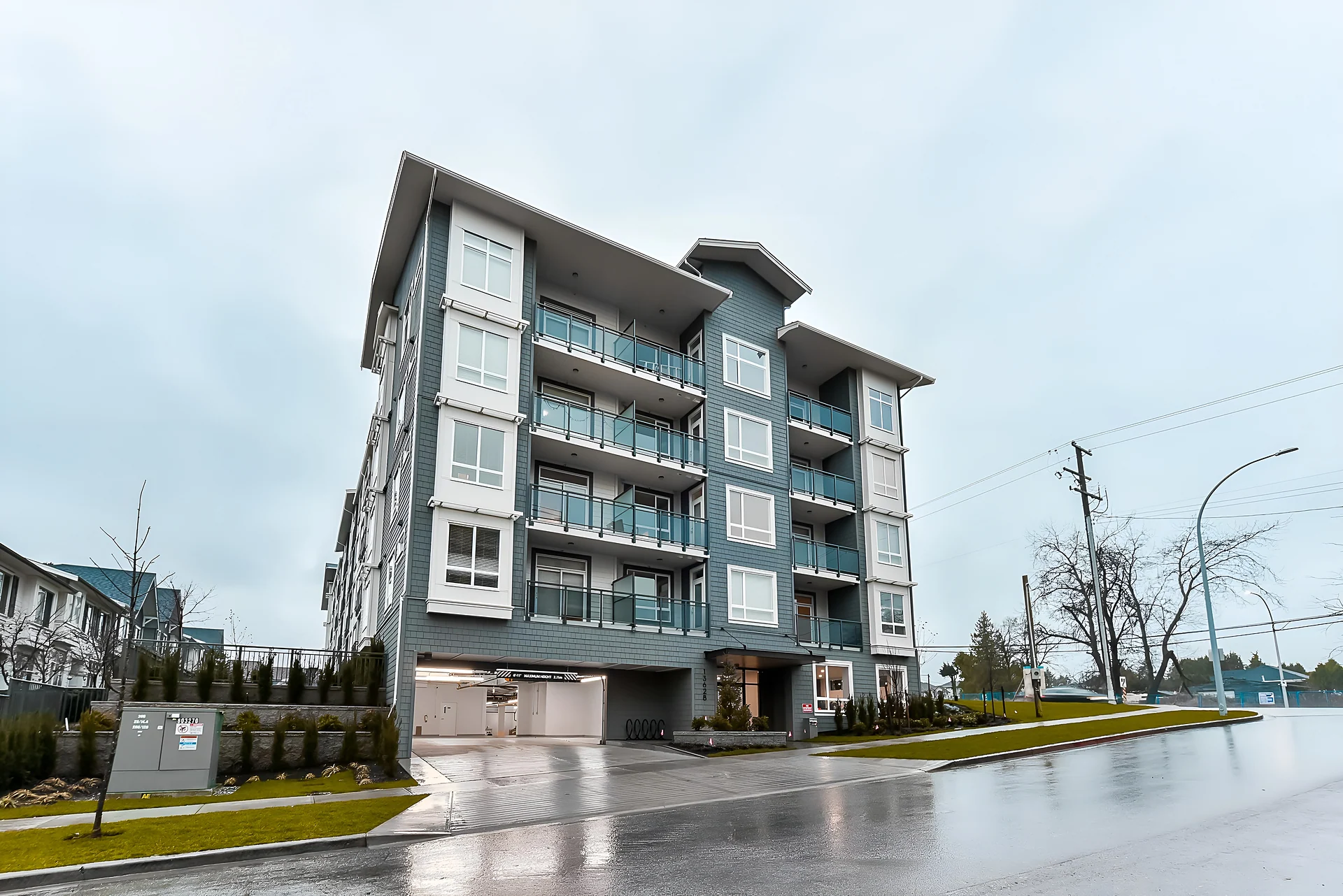 Five-storey blue-grey residential condo building with balconies on a wet overcast day
