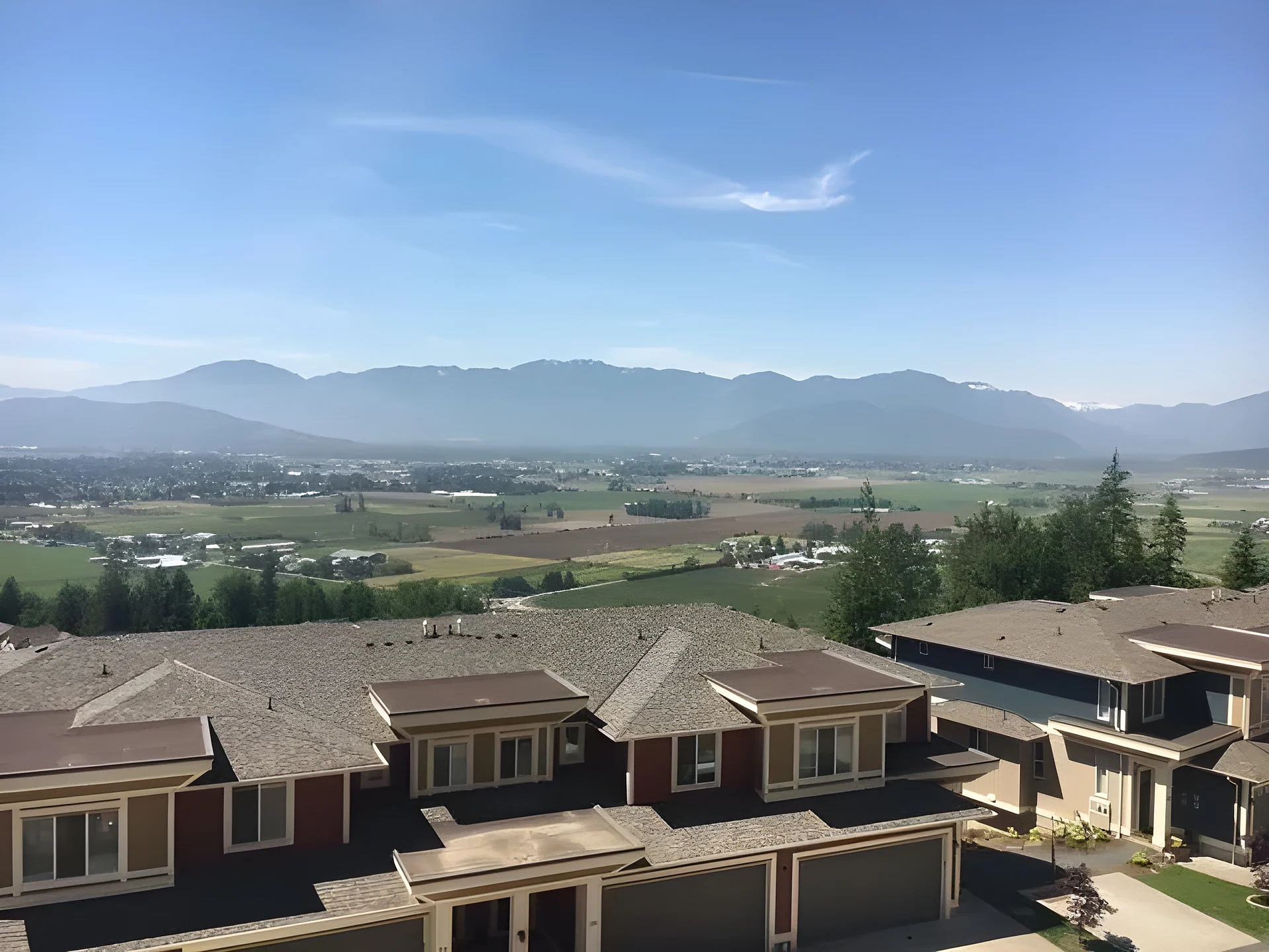Elevated view over townhouse roofs to a flat valley with farmland and mountains beyond