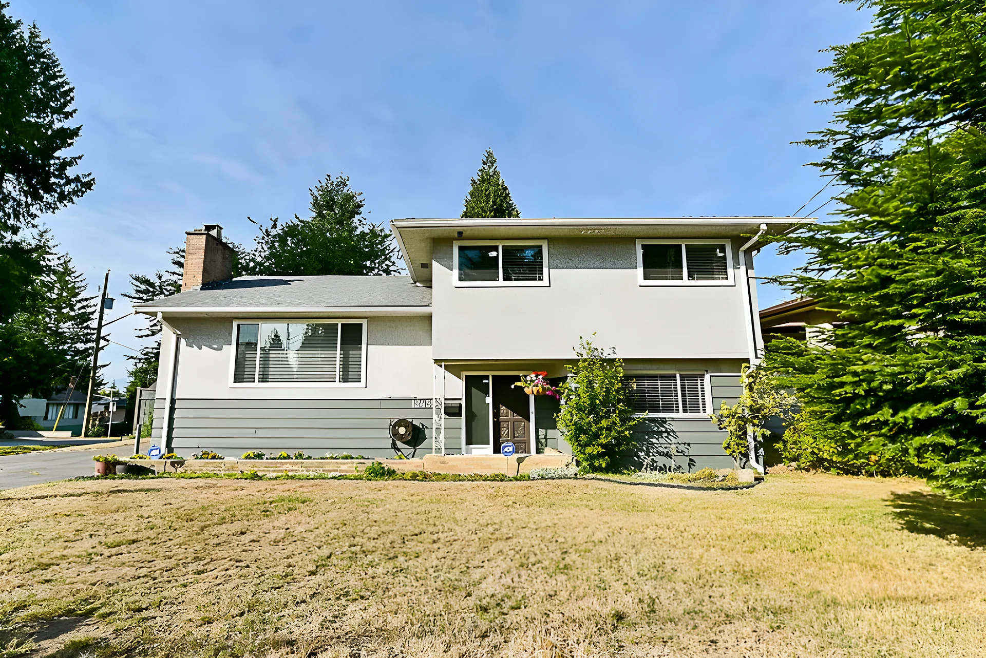 Split-level grey house with lawn, large trees and blue sky