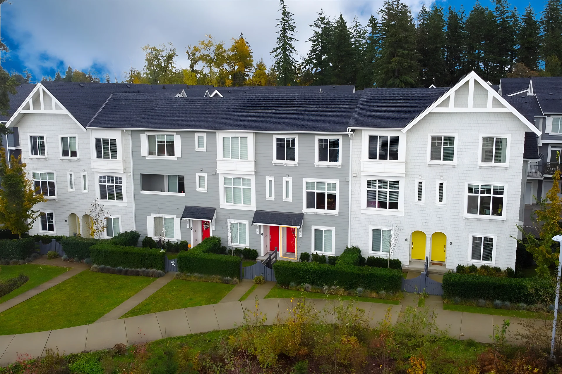 Aerial view of grey townhouses with red and yellow doors, lawns and walkways