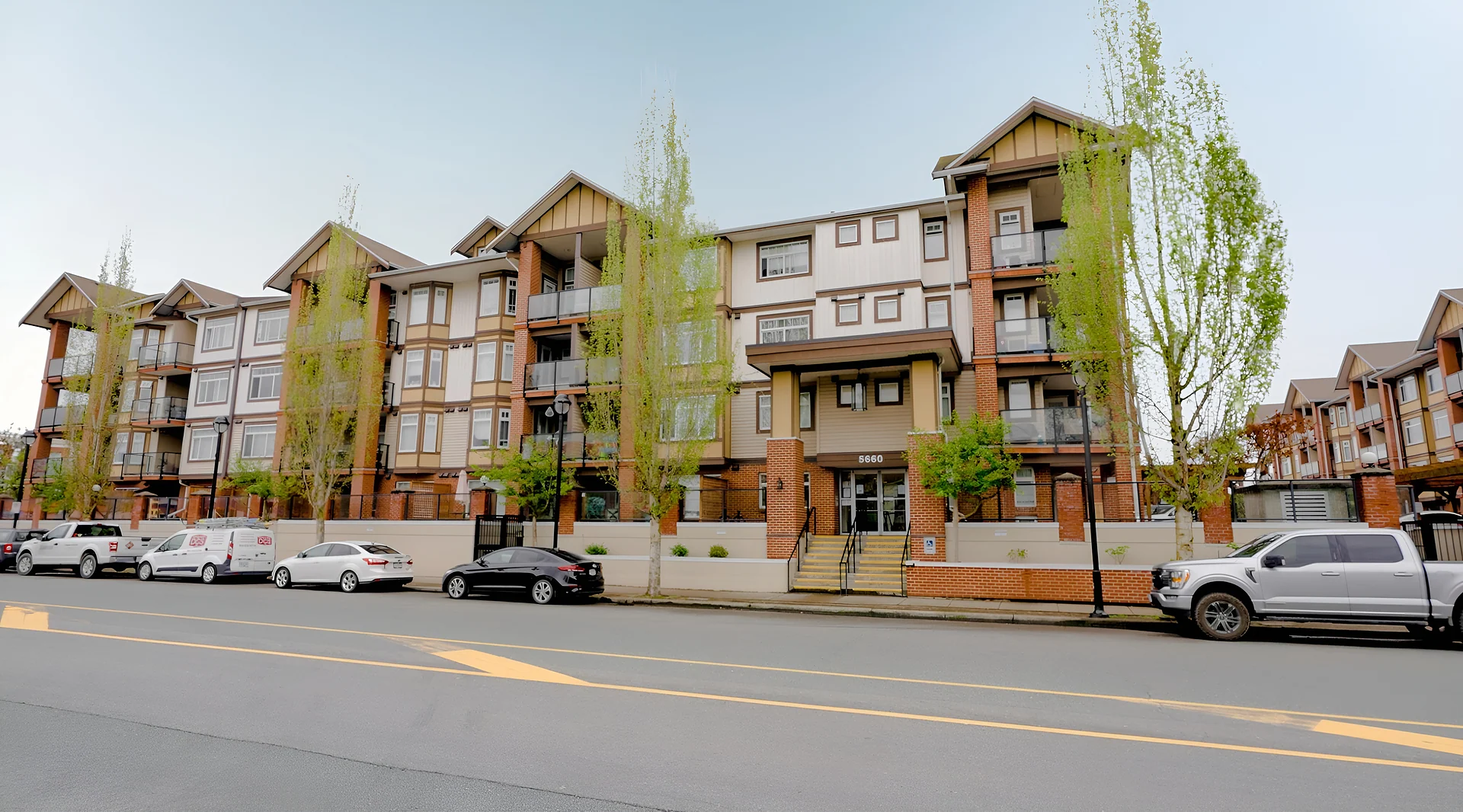 Four-storey brown and tan condo building with balconies on a street with parked cars