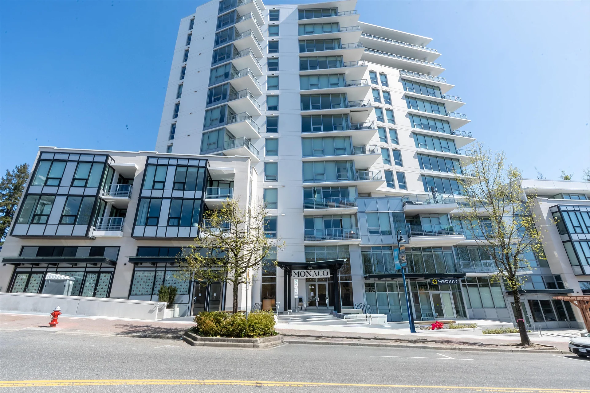 Tall white-and-glass residential tower with retail podium at street level, blue sky