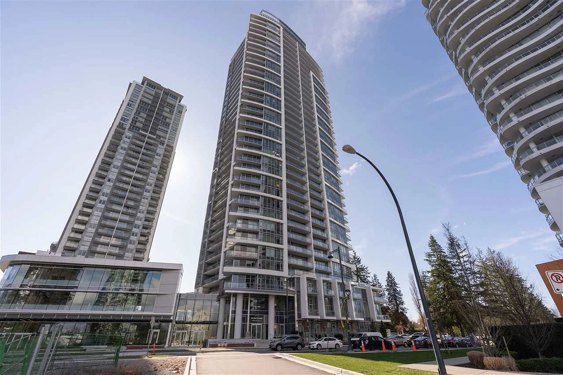 Tall residential glass tower viewed from street, blue sky
