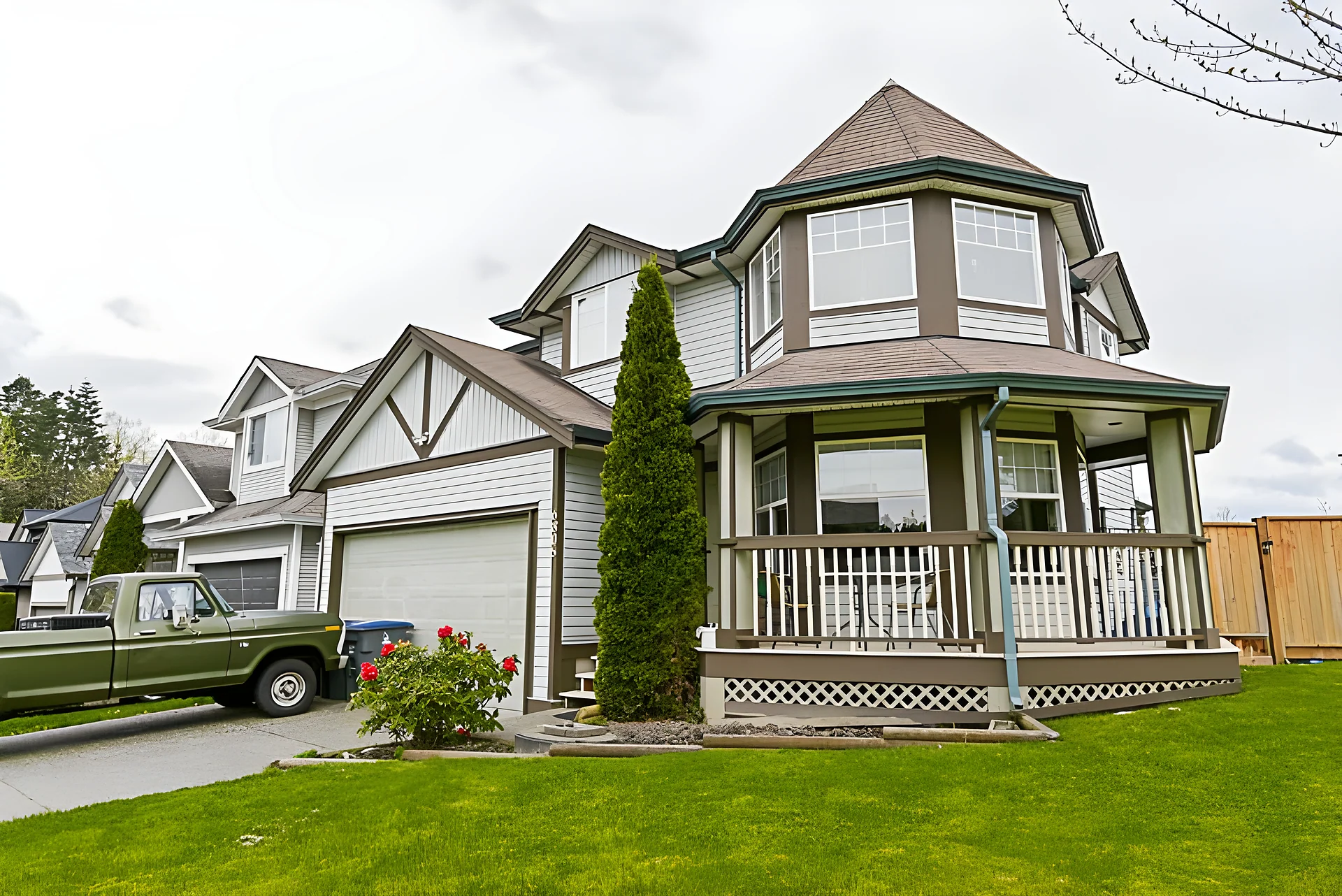 Two-storey house with covered front porch and turret-style upper window, green lawn, old green pickup truck at left