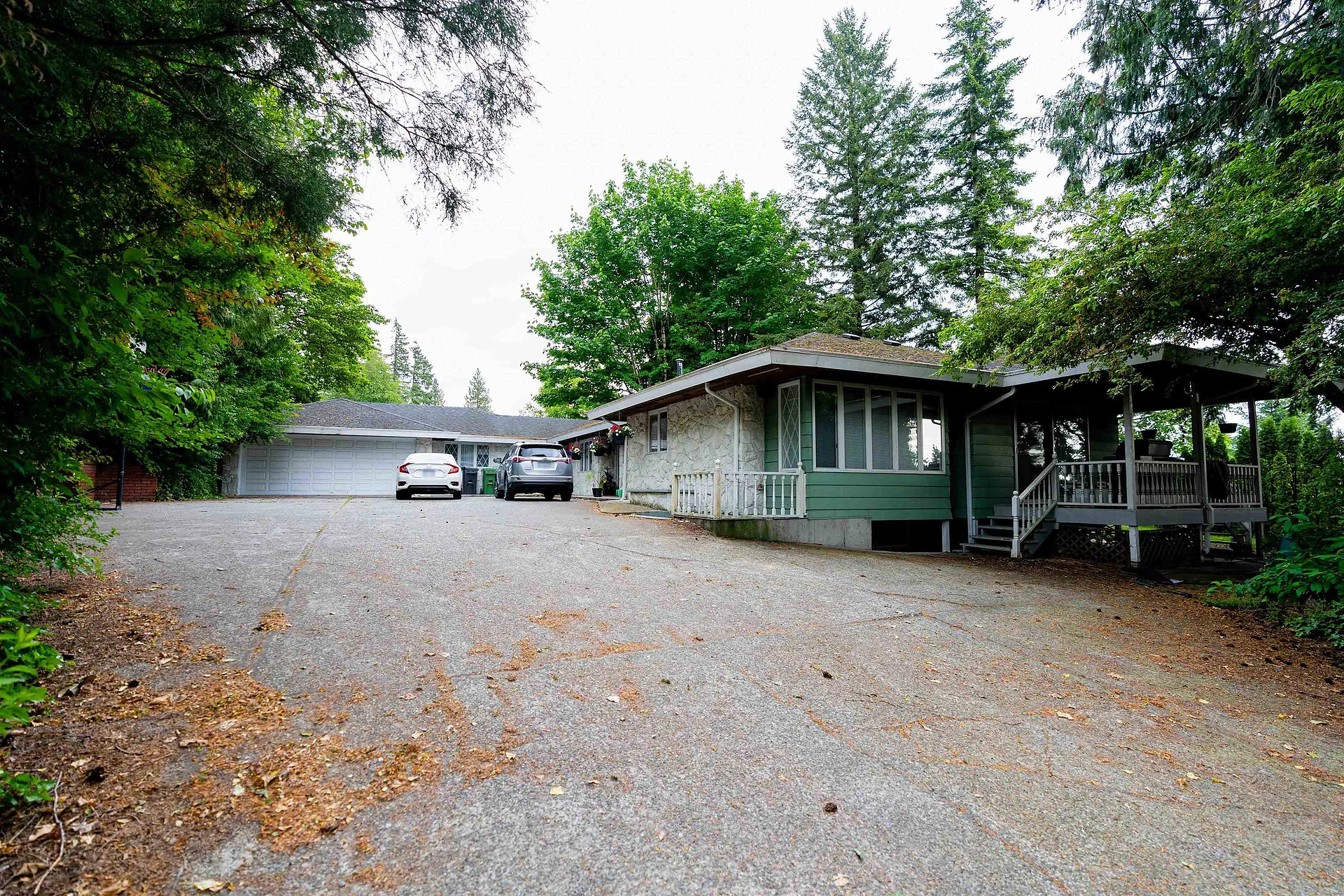 Single-storey home with green accents and large gravel driveway among trees