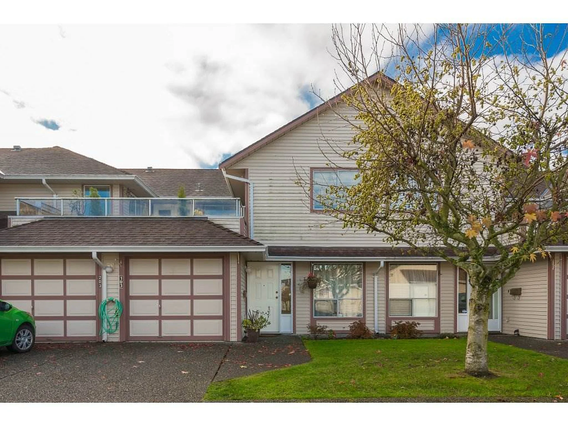 Attached two-storey home with two garage doors, bare tree and lawn