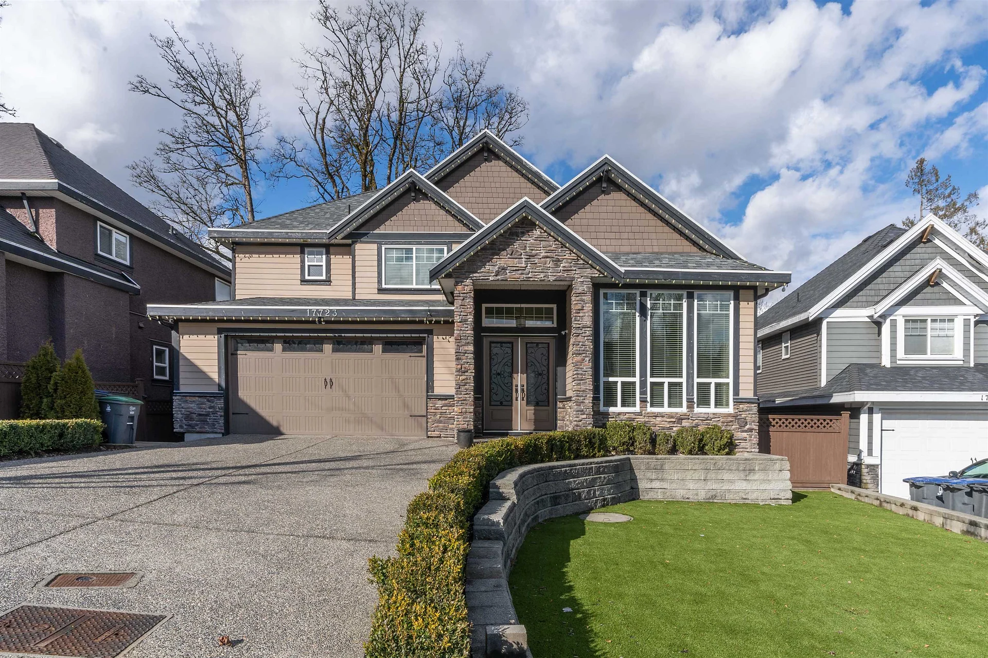 Large two-storey house with stone accents, a double garage and a driveway under a cloudy sky