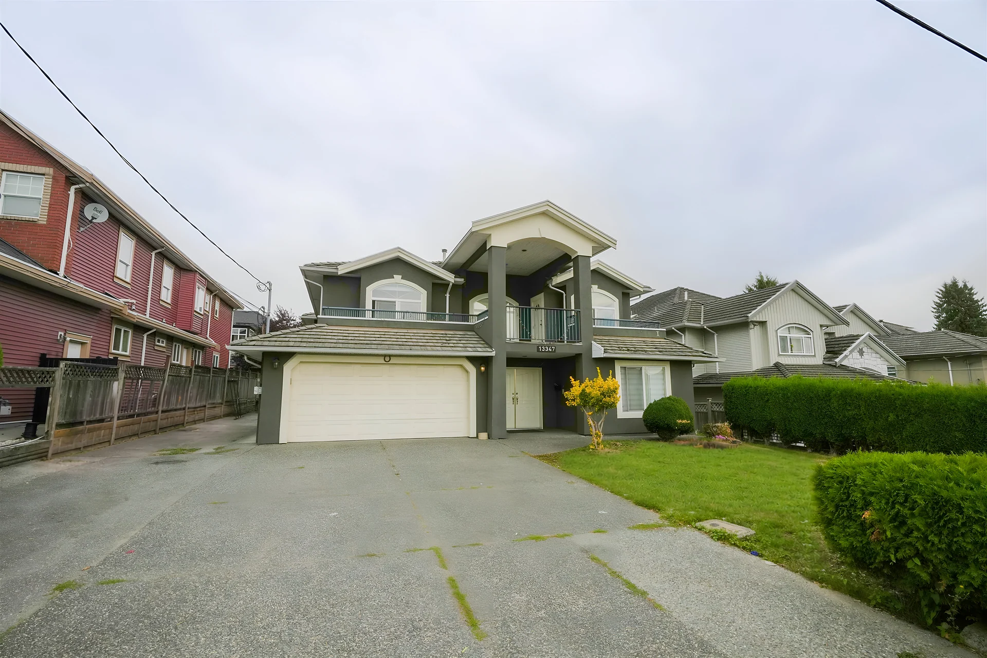 Two-storey grey-green house with double garage and an empty driveway under an overcast sky