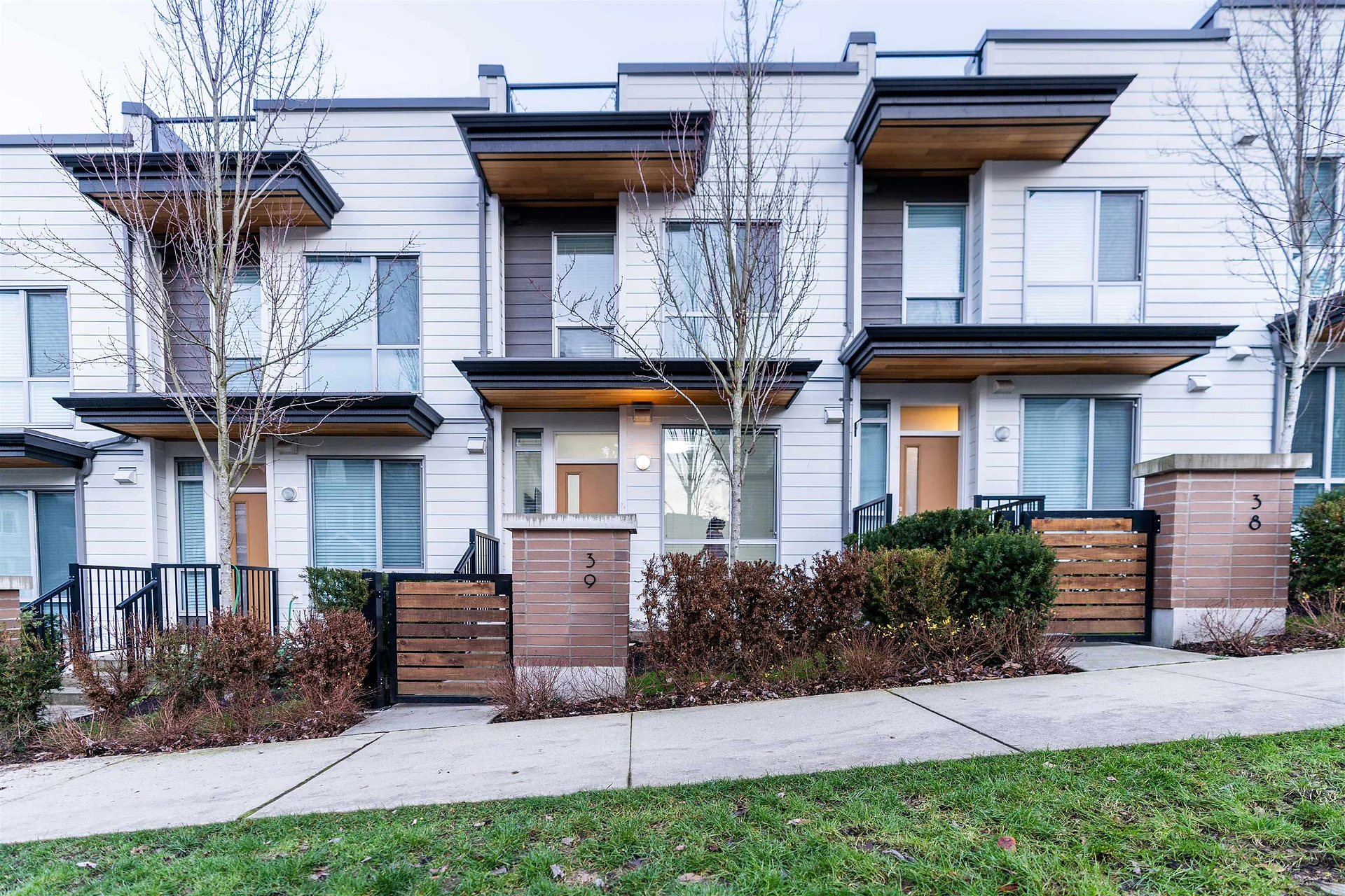 Row of modern townhouses with grey siding, balconies and wooden fences along a sidewalk