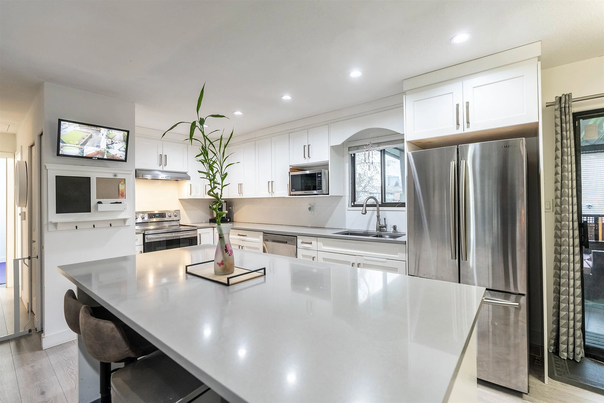 Bright white kitchen with island, stainless fridge and bar stools