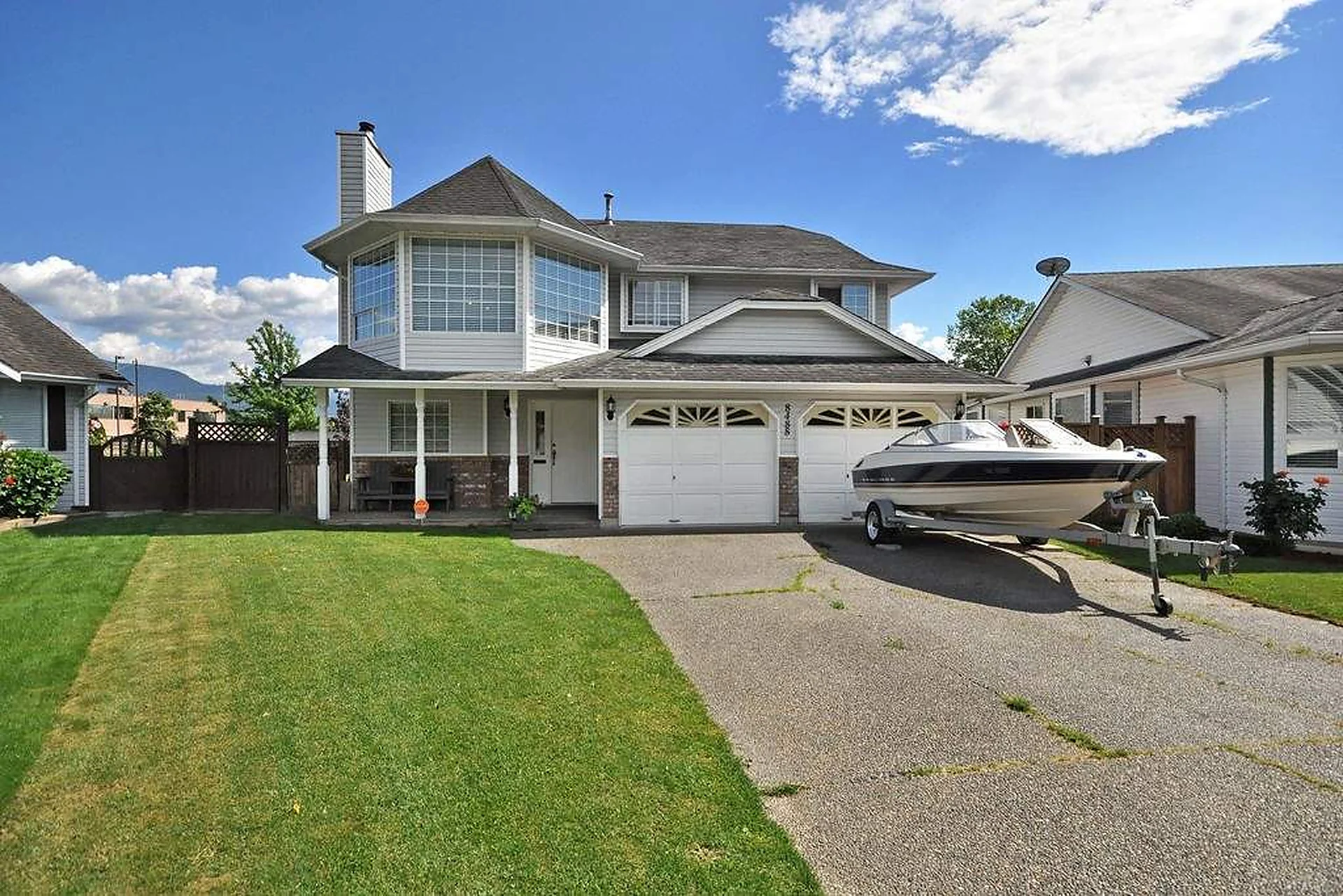 Two-storey white house with double garage and boat on trailer in driveway, green lawn, blue sky