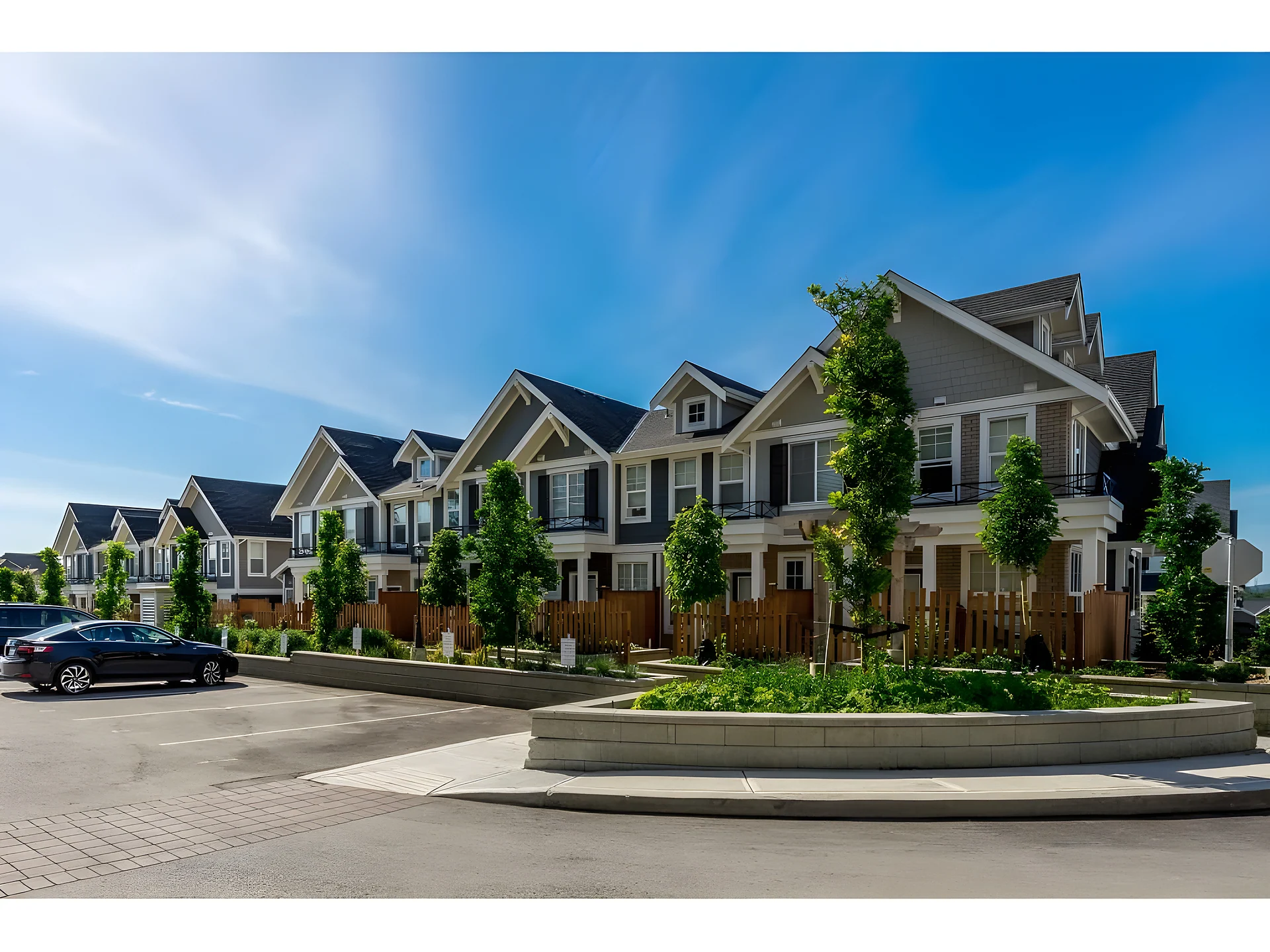 Row of new beige and grey townhouses with landscaped courtyard and a parked car on a sunny day