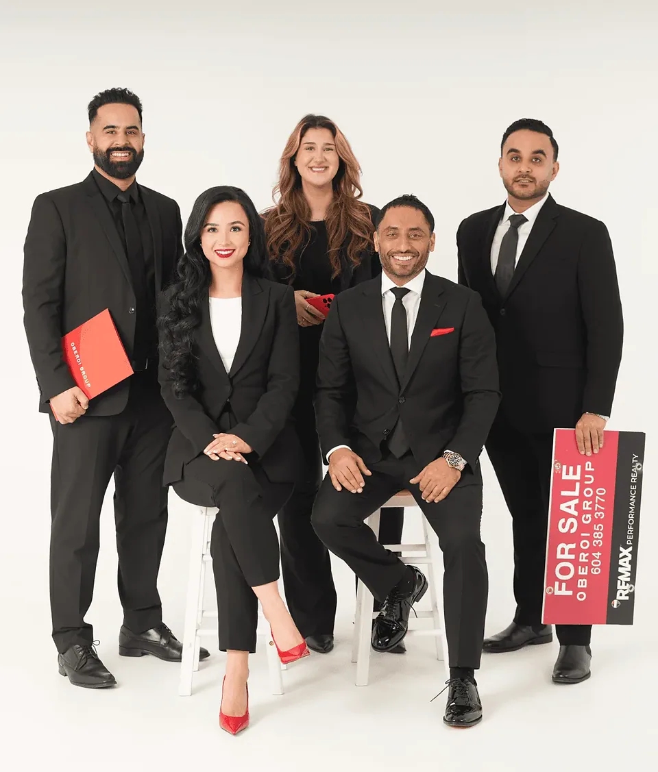 Five members of The Oberoi Group in black outfits in a white studio, one holding a red For Sale sign