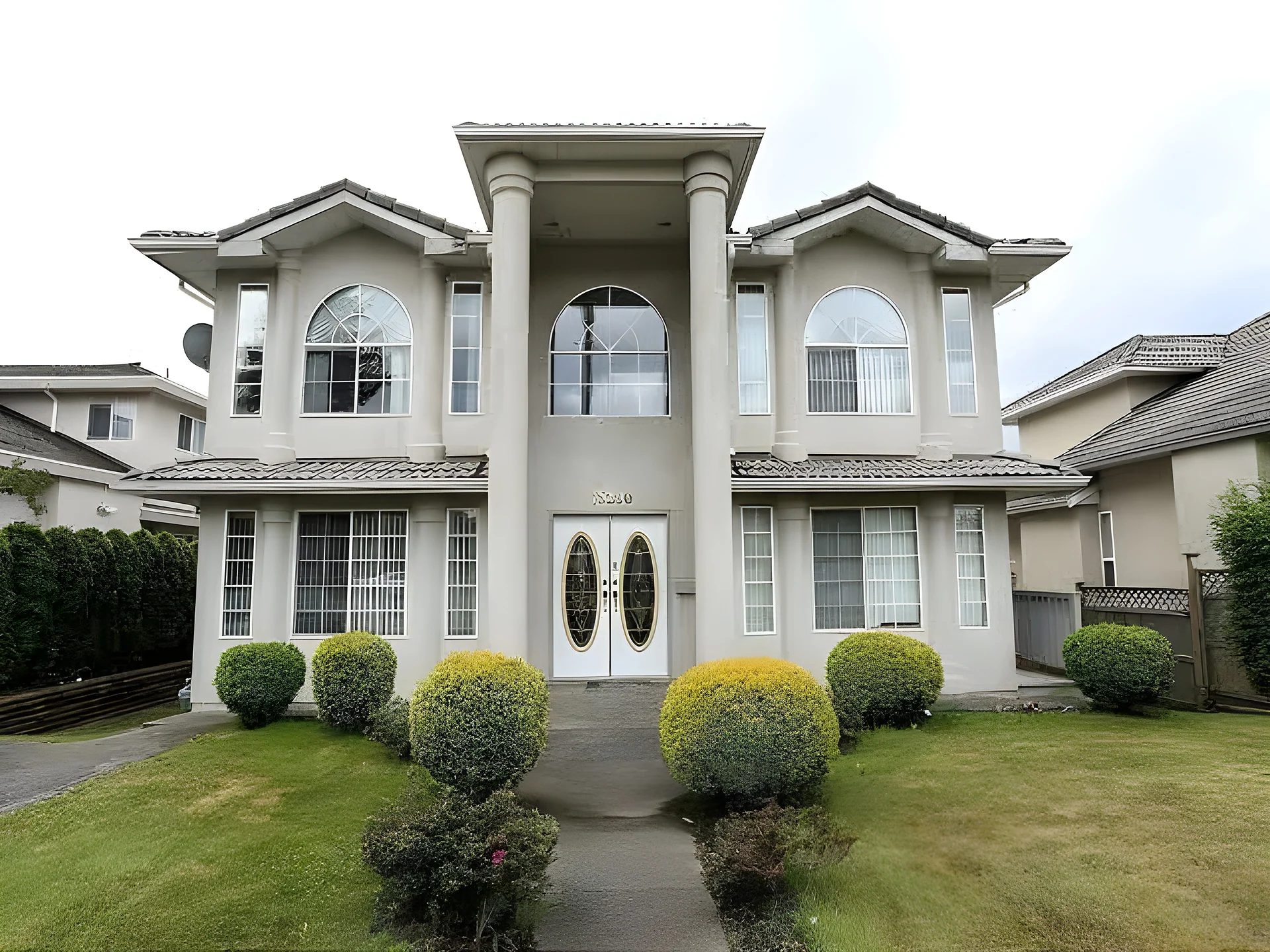 Large two-storey stucco house with columns, arched windows, double front door and trimmed hedges