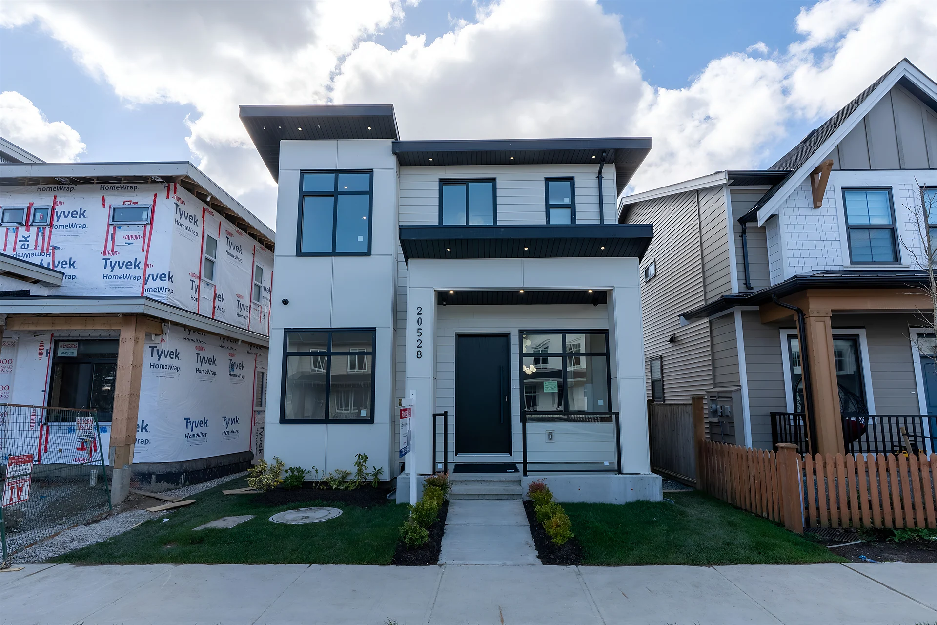 New two-storey white and grey house beside a home under construction
