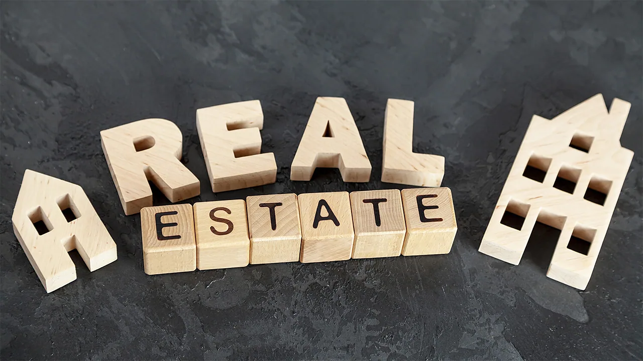 Wooden letter blocks spelling REAL ESTATE with house shapes on dark slate
